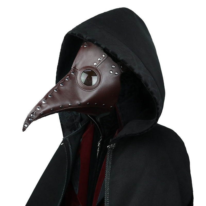 Brown plague doctor mask with rivets worn over black hooded cloak | Chaps London