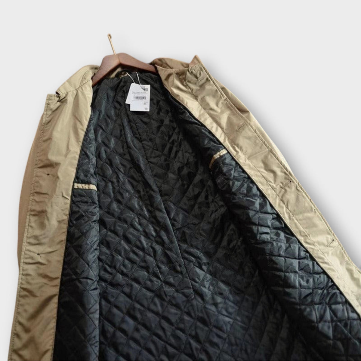 Beige rain mac on hanger showing black quilted lining detail | Chaps London