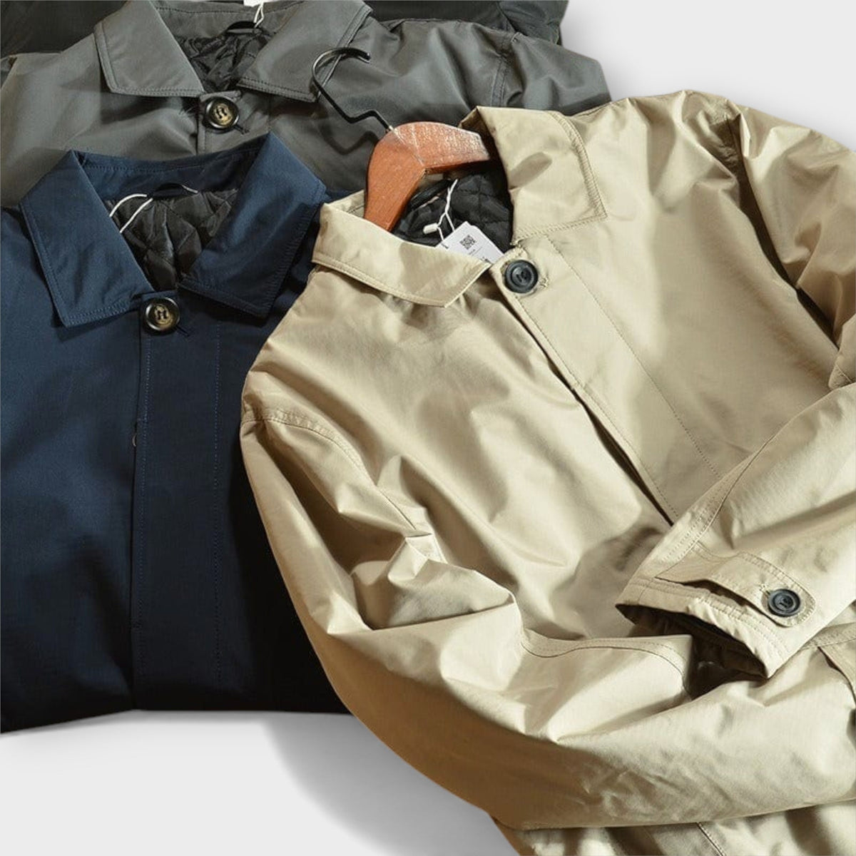 Beige, navy, and olive button-front rain macs stacked flat, folded overlapping | Chaps London