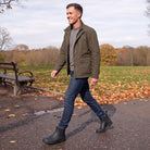 Man walking through an autumn park in black Chelsea wellies, jeans and an olive jacket