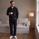 Man wearing black quarter zip sweatshirt and joggers, holding coffee mug indoors | Chaps London