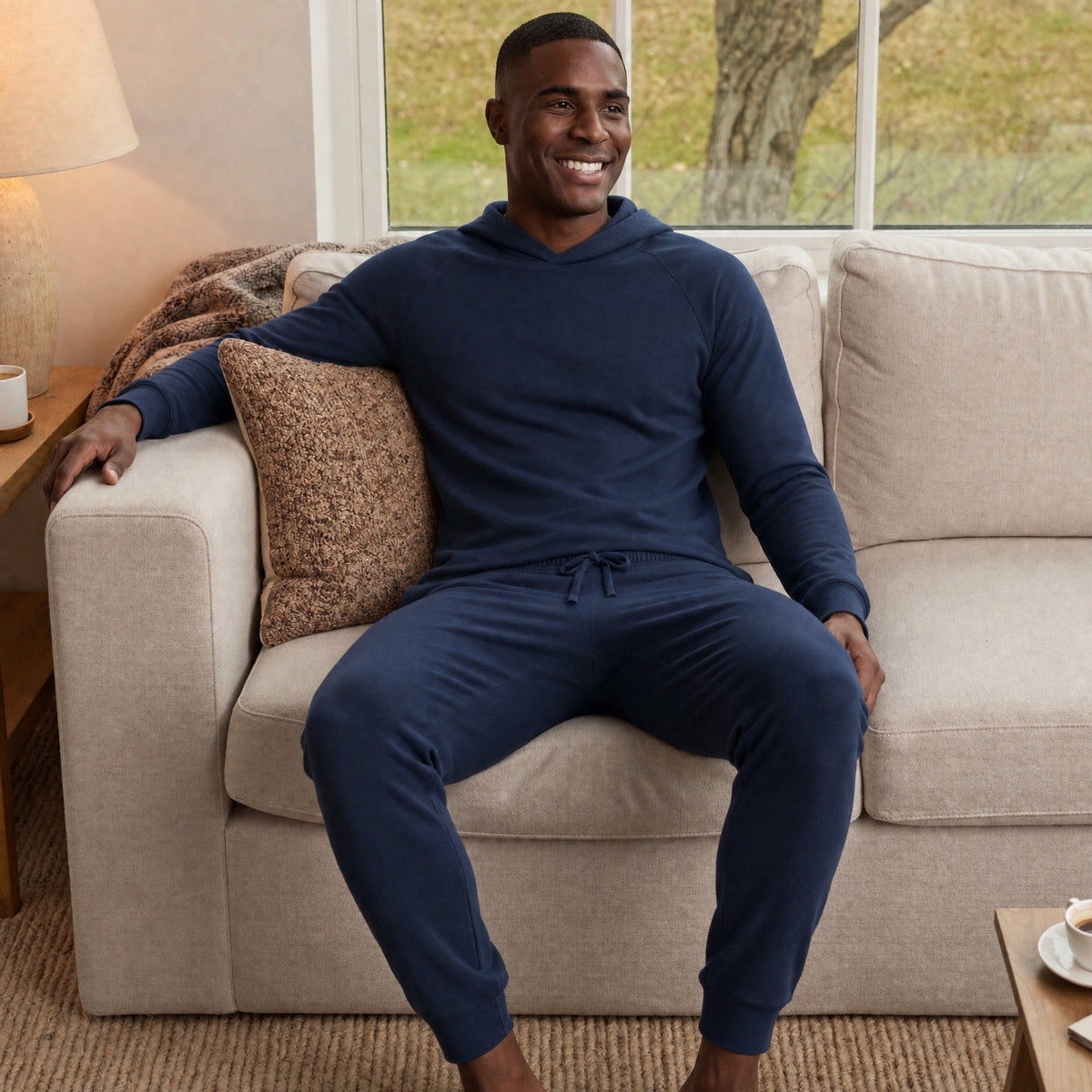 Man wearing navy hoodie and joggers, seated on beige couch | Chaps London