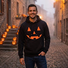 Man wearing black hoodie with orange jack-o-lantern face on cobblestone street | Chaps London