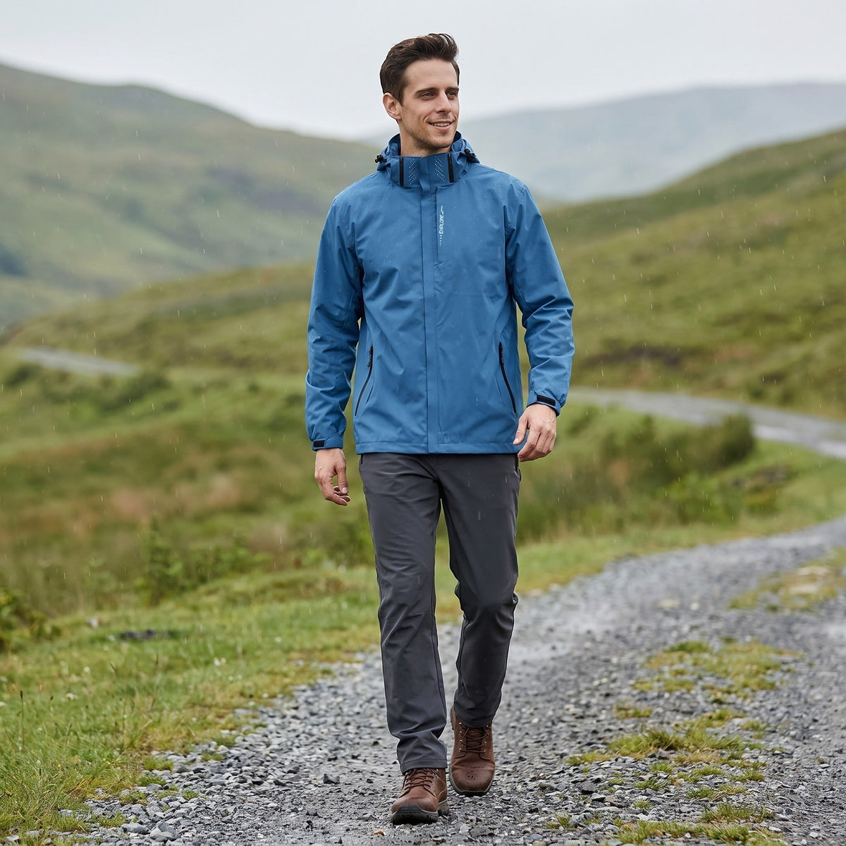 Man wearing blue waterproof hooded rain jacket, walking on gravel path outdoors | Chaps London