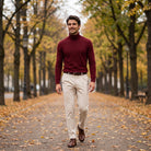 Man wearing burgundy ribbed turtleneck jumper with beige trousers, walking on tree-lined path | Chaps London