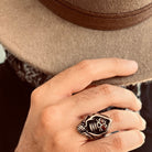 Silver skull ring with red eyes worn on finger near hat | Chaps London