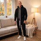Man wearing black hoodie and joggers tracksuit in living room | Chaps London