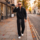 Man wearing black striped half zip tracksuit with wide leg trousers outdoors | Chaps London