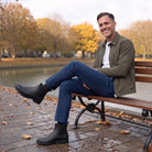 Man sitting on a bench by a canal wearing black Chelsea wellies