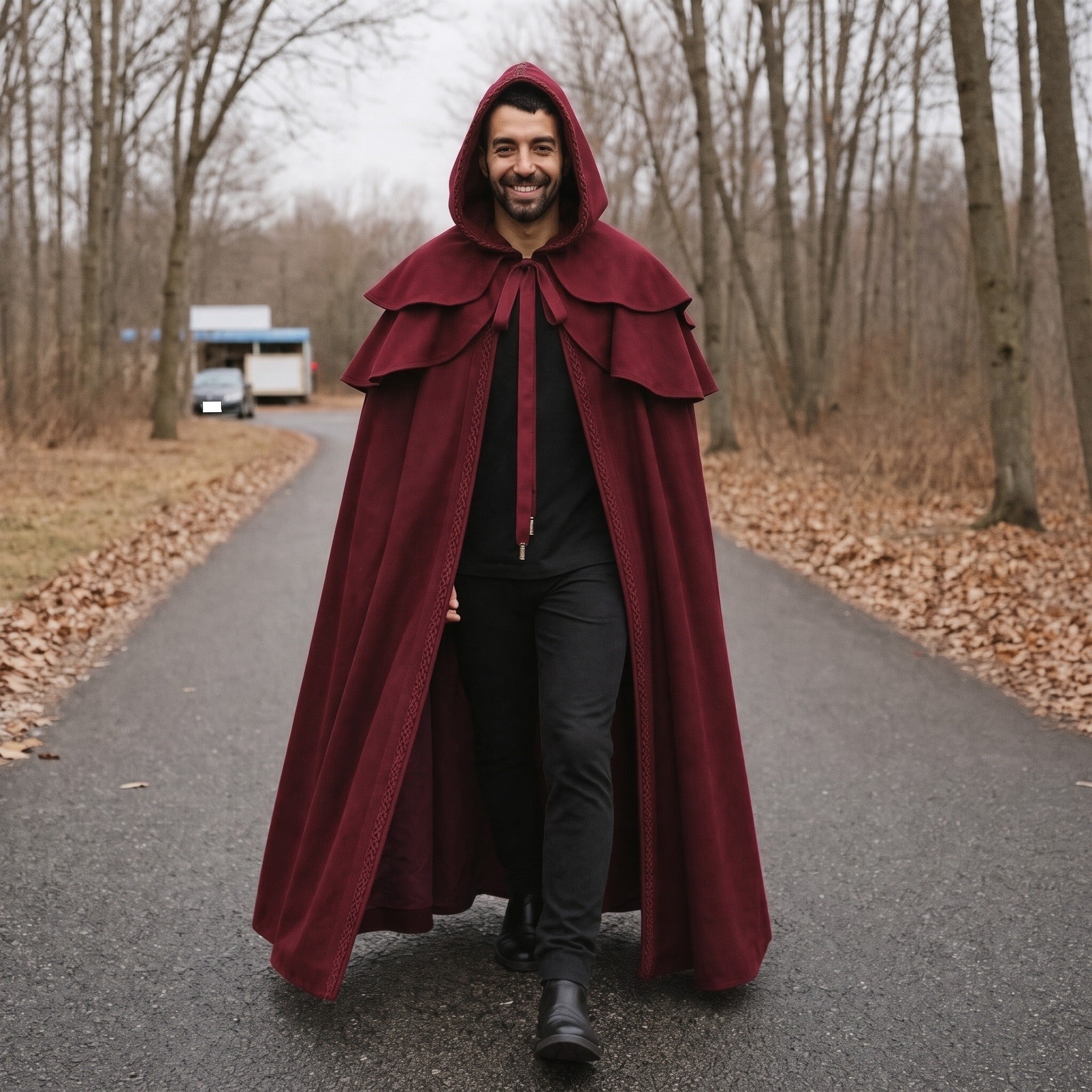 Man wearing burgundy hooded cape with layered collar, walking outdoors on path | Chaps London