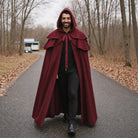 Man wearing burgundy hooded cape with layered collar, walking outdoors on path | Chaps London