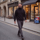 Man wearing black oversized roll neck jumper with grey trousers, walking outdoors | Chaps London