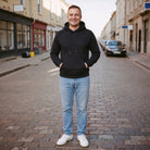 Man wearing black drawstring hoodie with light blue jeans on cobblestone street | Chaps London