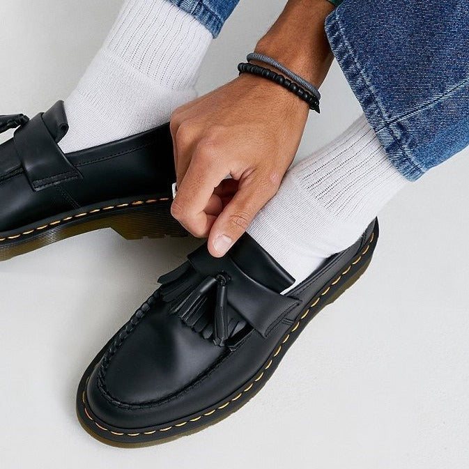 Men's black tassel loafers with a chunky sole, worn with white socks and jeans