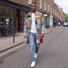 Man walking on a London street in a mid-length open front coat with a colourful hand sign print, white T-shirt and light jeans