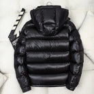 Black shiny hooded puffer jacket, back view, laid flat on cushion | Chaps London