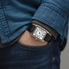 Rectangular watch with a black strap worn on the wrist with a denim shirt