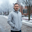 Man wearing light gray hooded jacket, standing on snowy cobblestone street | Chaps London