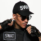 Man wearing black SWAT cap, vest, and fingerless gloves, touching earpiece | Chaps London