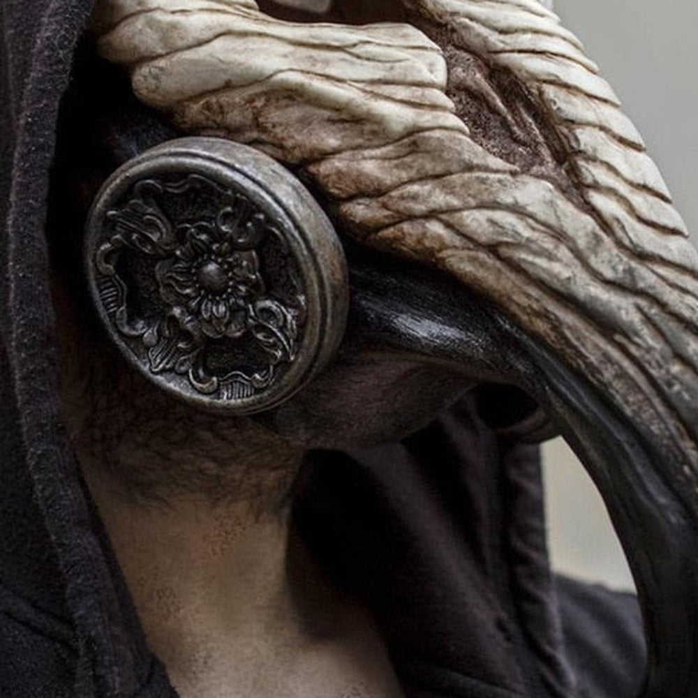 Worn raven mask close-up showing textured beak and ornate metal ear disc | Chaps London