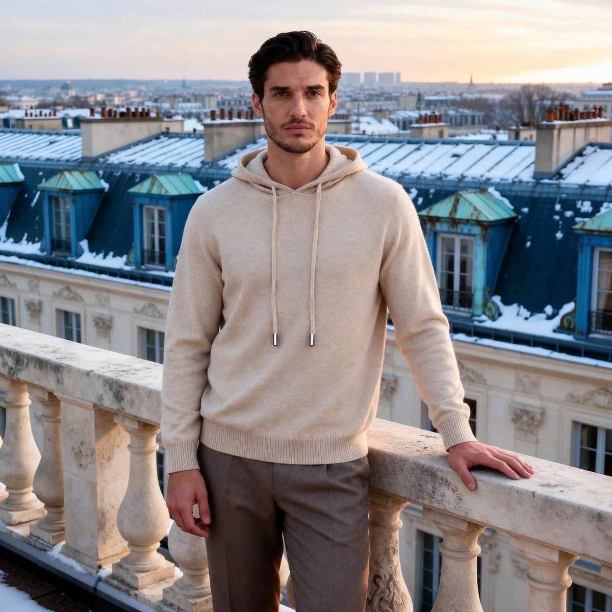 Man wearing beige knit hoodie on balcony overlooking snowy rooftops | Chaps London