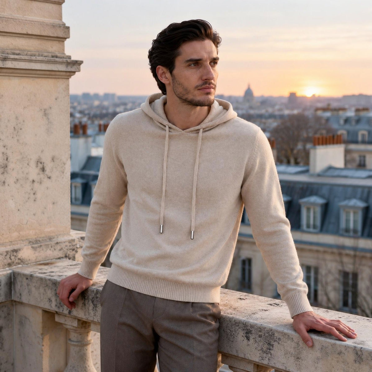 Man wearing beige knit hoodie on balcony overlooking city at sunset | Chaps London
