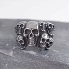 Silver skull ring with multiple skulls, shown flat on dark stone surface | Chaps London