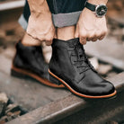 Black lace-up ankle boots worn by person standing on railroad tracks | Chaps London