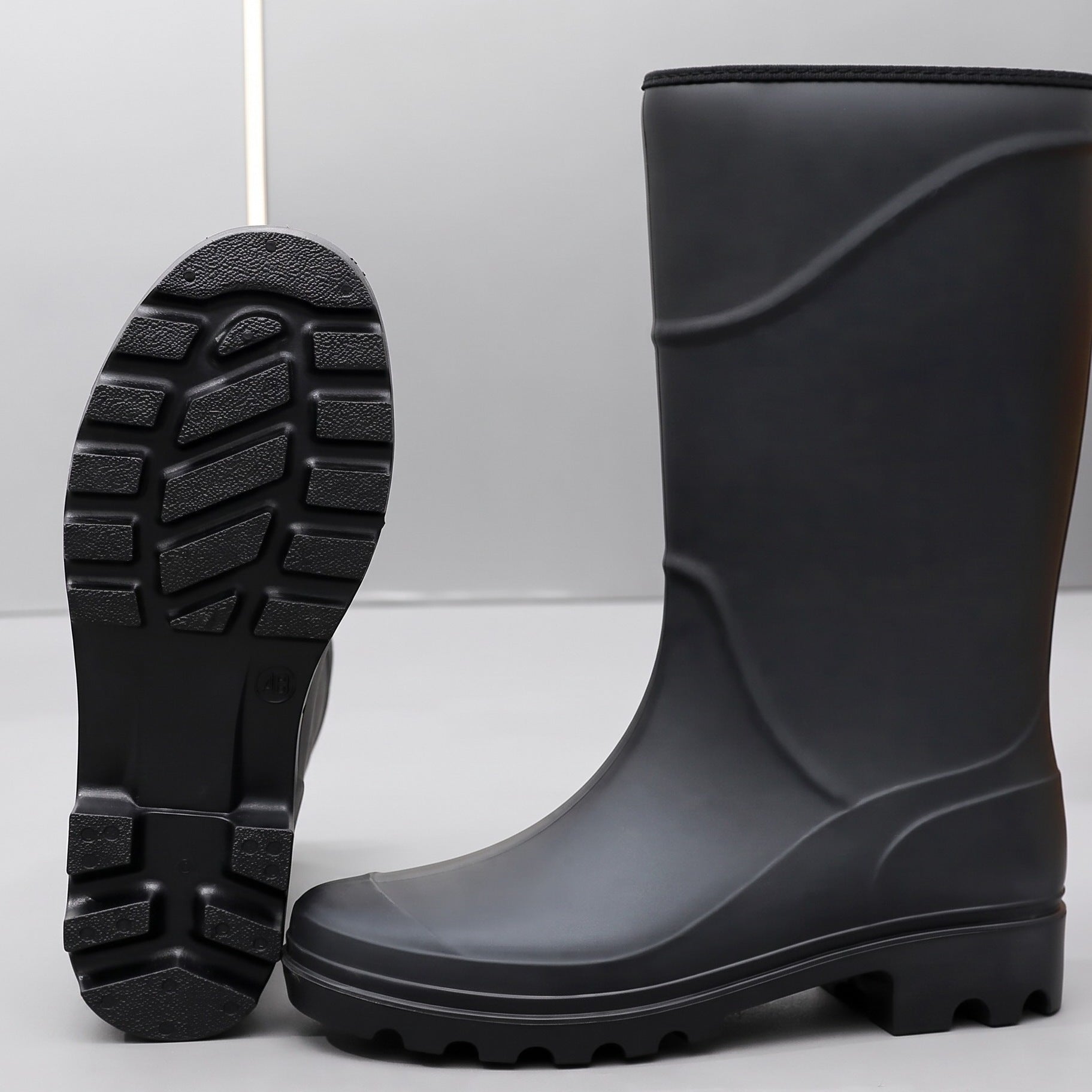 Black mid-calf rubber boots, one upright, one showing textured sole tread | Chaps London