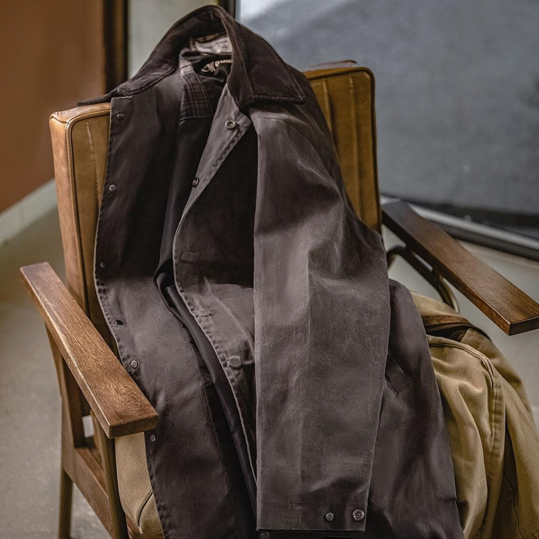 Brown waxed jacket with corduroy collar draped open over wooden chair | Chaps London