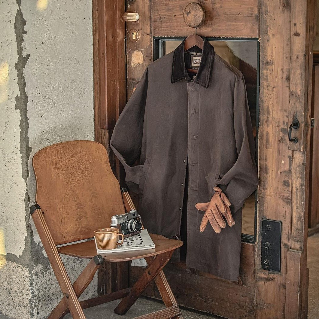 Brown waxed jacket with corduroy collar hanging on wooden door, gloves beneath | Chaps London