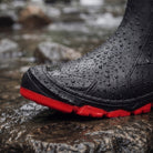 Black rain boot with red treaded sole on wet rock | Chaps London
