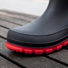Close-up of black mid-calf welly toe with red textured sole, worn, outdoors | Chaps London