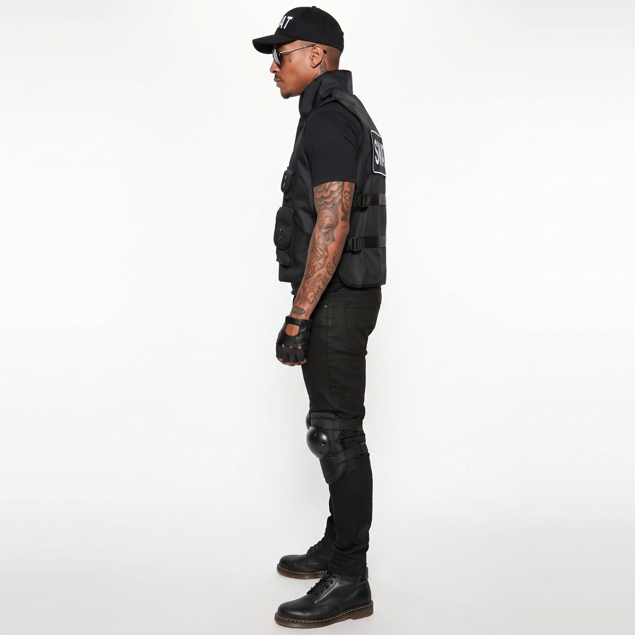Man wearing black tactical vest, cap, gloves, and knee pads, side view | Chaps London