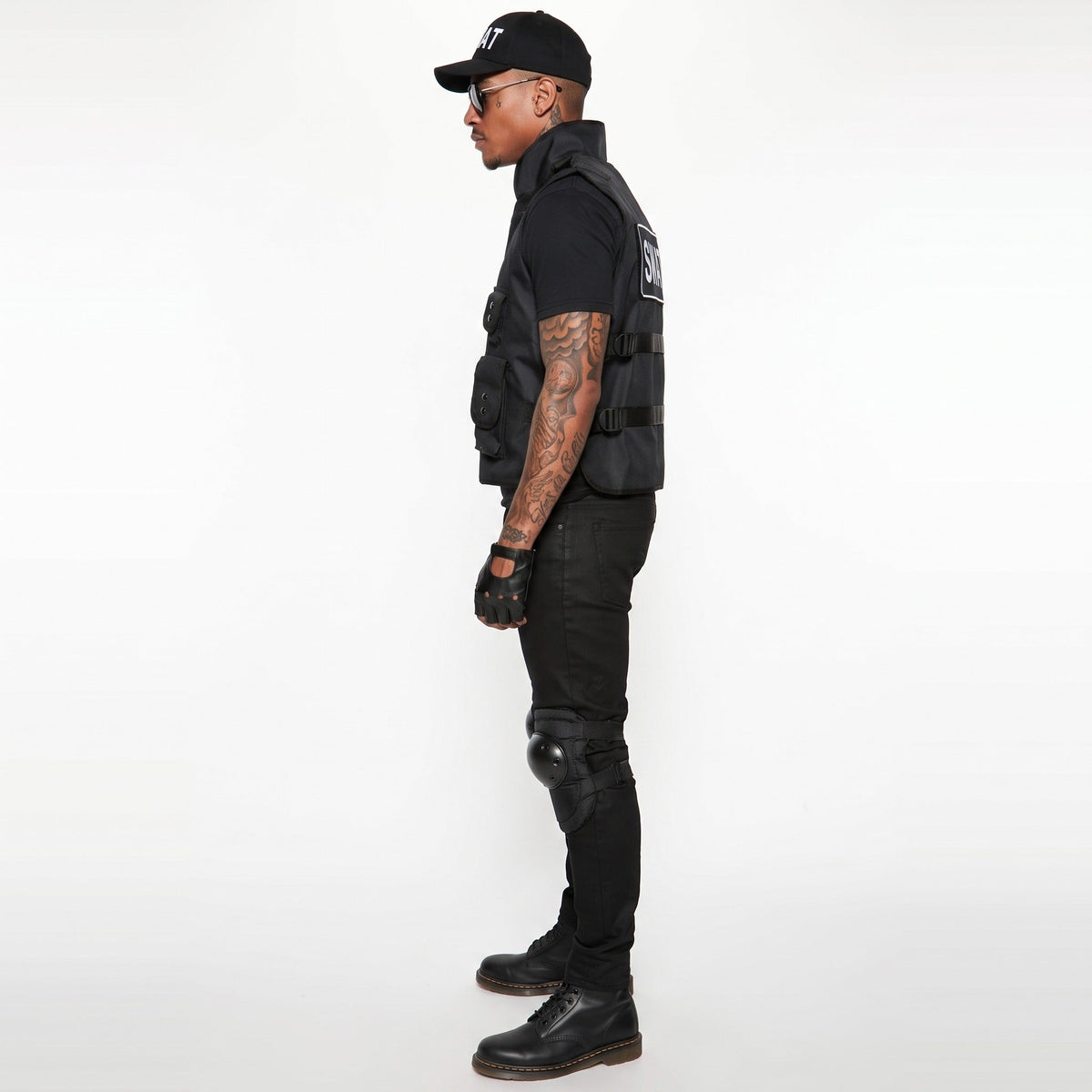 Man wearing black tactical vest, cap, gloves, and knee pads, side view | Chaps London