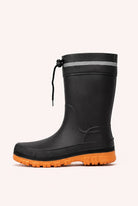 Side view of a black mid calf rain boot with an orange lugged sole, a reflective band and a drawstring at the top.
